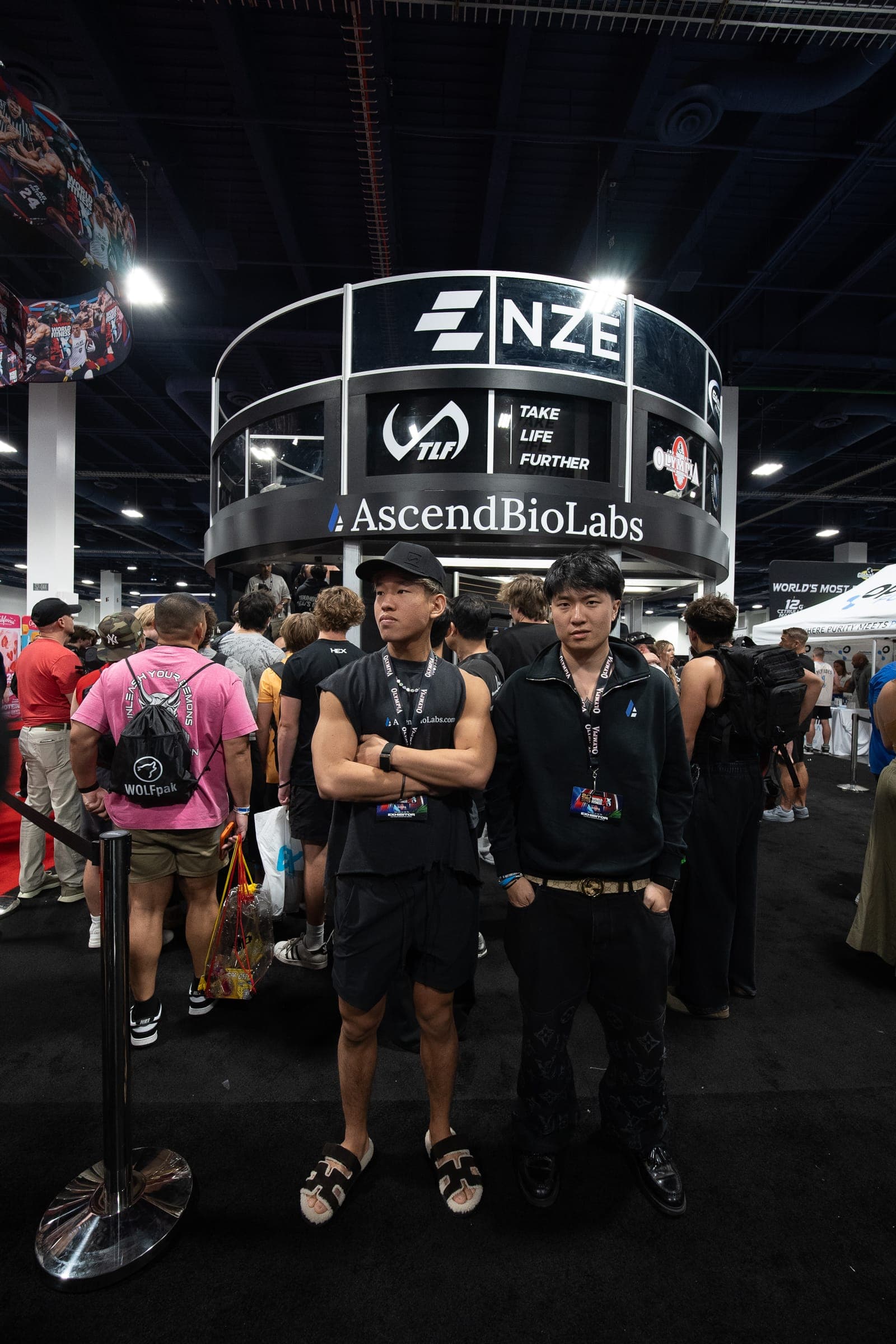 Two men stand in front of the AscendBioLabs booth at a busy trade show.